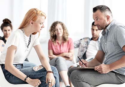 Adolescent teen woman sits with counselor during a group therapy session in mental health rehab.