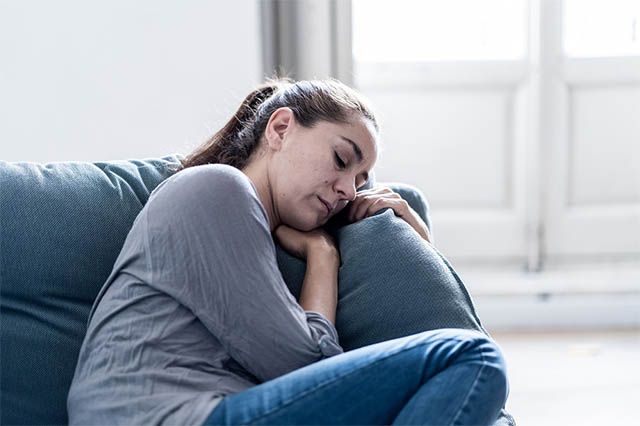 A woman sits with her head down on the couch showing cocaine withdrawal symptoms.