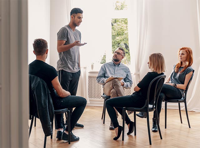 A young man stands up for recognition during an addiction and mental health group therapy session.