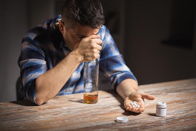 A man takes prescription pills with alcohol, one of the signs of prescription drug abuse.