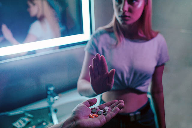 A young woman recovering from addiction holds up her hand, saying no when offered drugs, avoiding relapse.