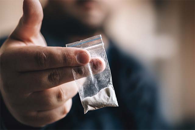 A man holds a small bag of cocaine in front of the camera.