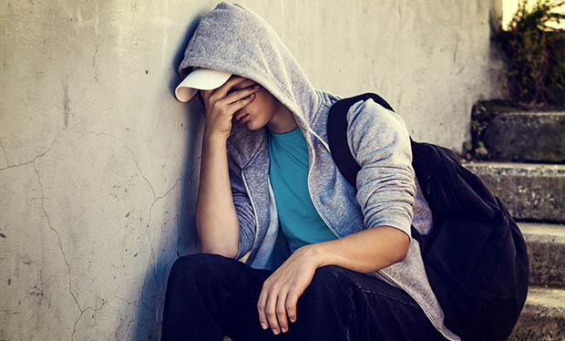 A young adult experiencing mental health issues sits on a staircase with his hand covering his face.