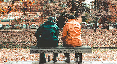 A man helps another to recover from his addiction as they sit on a park bench talking