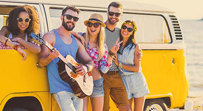 A group of friends at a California beach gather around a guitar to play and listen to music.