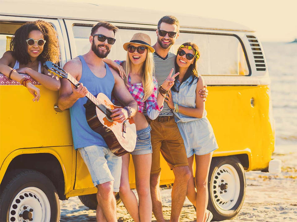 A group of friends at a California beach gather around a guitar to play and listen to music.