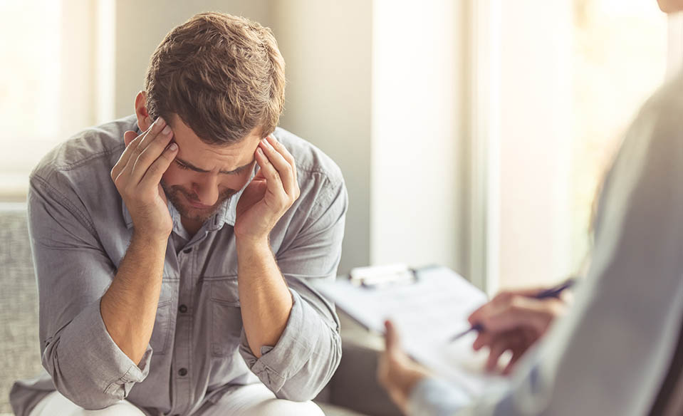 A man leans with his elbows on his knees as he talks to his therapist at an alcohol rehab center.