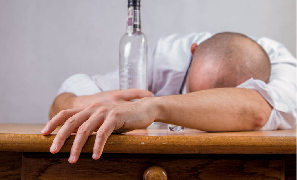 A man holds a bottle of alcohol while clearly suffering from alcohol poisoning.