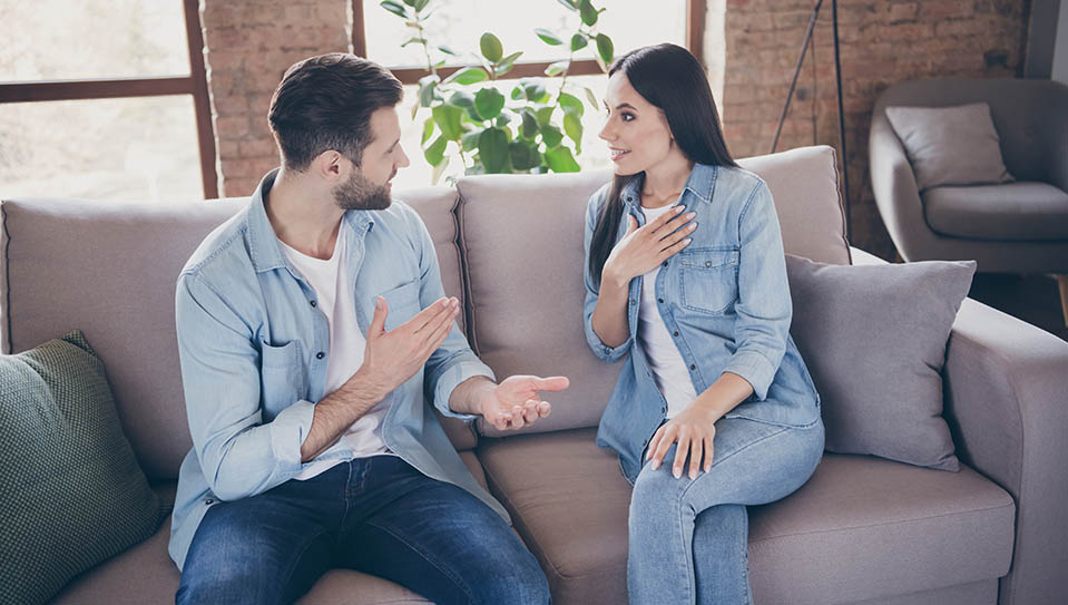 A couple cheerfully communicates while sitting on a couch.