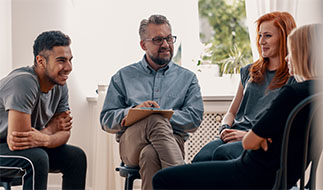 An outpatient addiction treatment group goes around the room sharing; checking in and updating the group on recent events in their lives.