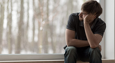 A depressed man struggling with addiction looks longingly out a window.