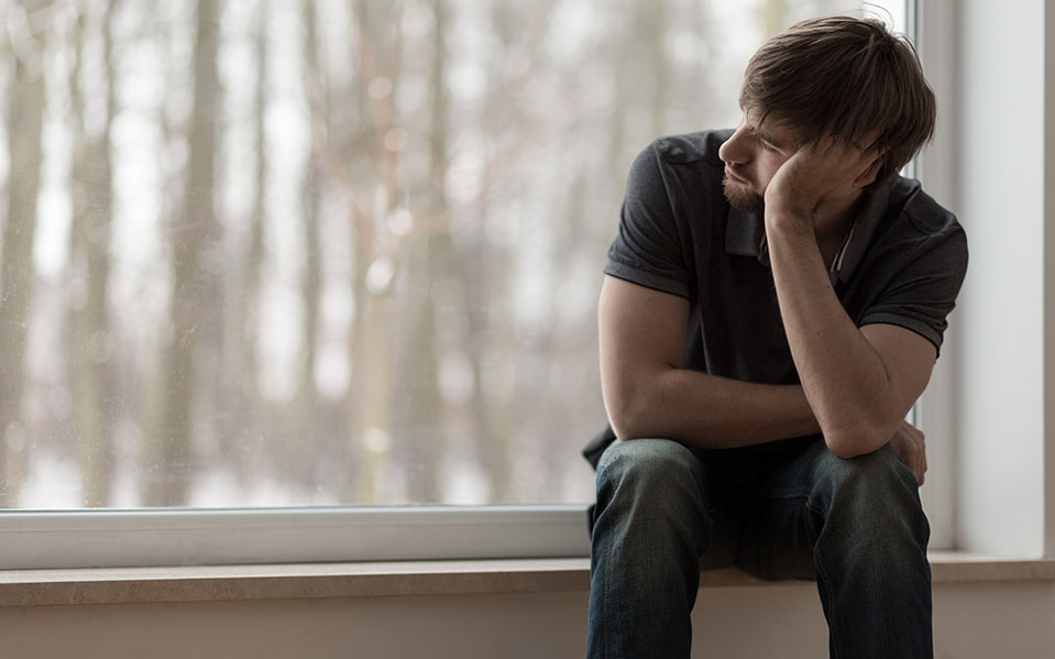 A depressed man struggling with addiction looks longingly out a window.