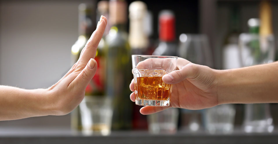 A hand out rejecting a drink of alcohol, symbolizing someone who is quitting drinking.