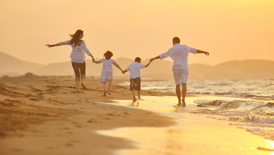 A family of four walks along the beach holding hands, becoming closer after family therapy.