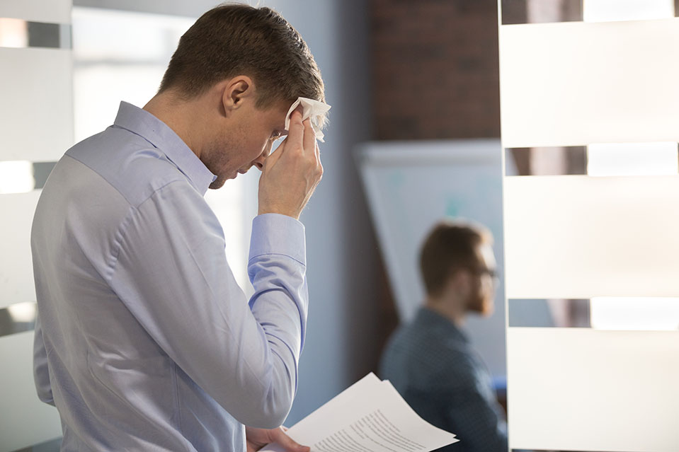 A man experiences opiate withdrawals while at work in early sobriety, sweating uncomfortably.