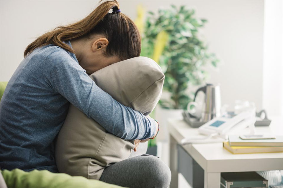 A young lady suffering from oxycodone addiction withdrawals leans forward with her head buried in a pillow.