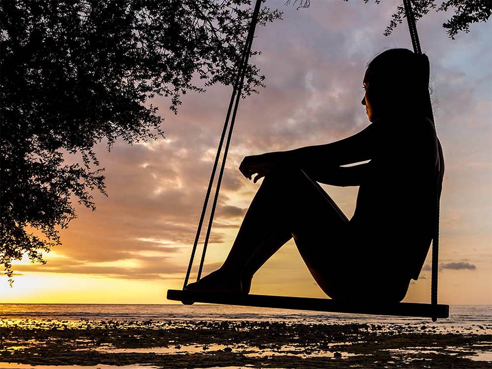 A sober woman sits on a swing by the ocean in California, thinking about her goals and dreams, or purpose in recovery.