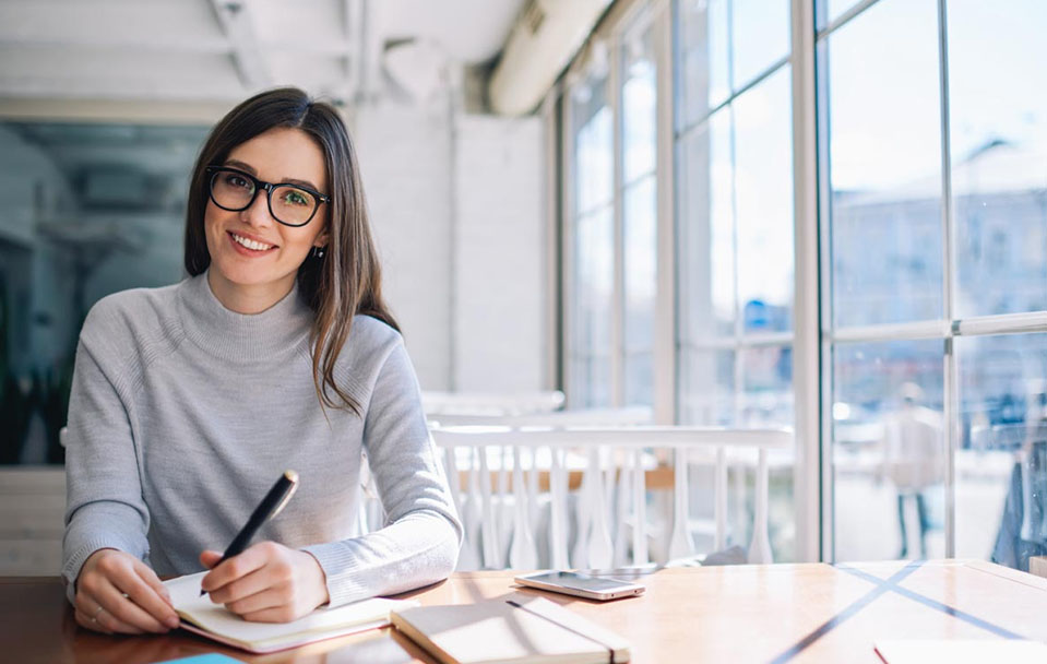 A woman smiles as she writes by a window, one of her hobbies that has replaced her addiction.