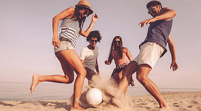 Family and friends enjoying a sober summer vacation, kicking a ball around on the beach.