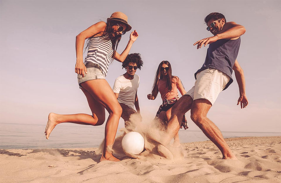 Family and friends enjoying a sober summer vacation, kicking a ball around on the beach.