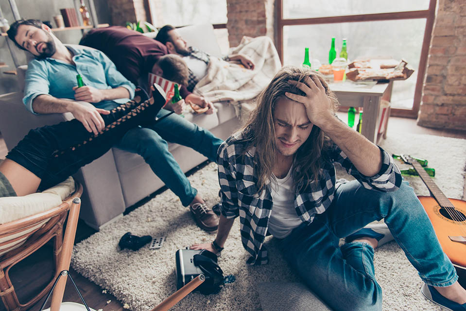 Man sitting on the floor after relapsing with his friends the night before, who are bad influences on his recovery.