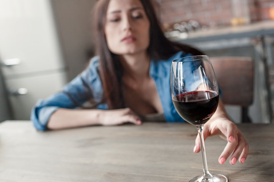 Sad woman reaching for wine glass, symbolizing answering the question of Does Alcohol Make You Depressed.