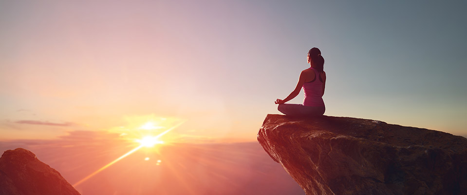 A woman practices yoga and meditates on a mountain as a healthy coping mechanism instead of drinking alcohol.