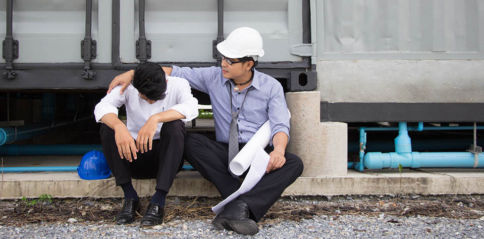 A coworker with his hand on his shoulder supporting another worker who is very stressed out.