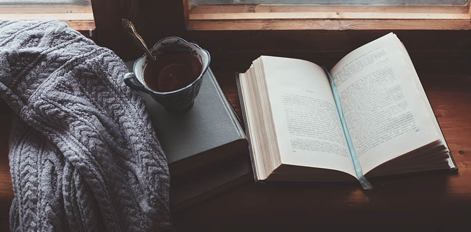 A book and a cup of hot tea sit invitingly on a window shelf. Reading can be a great tip for helping to deal with a lot of stress.