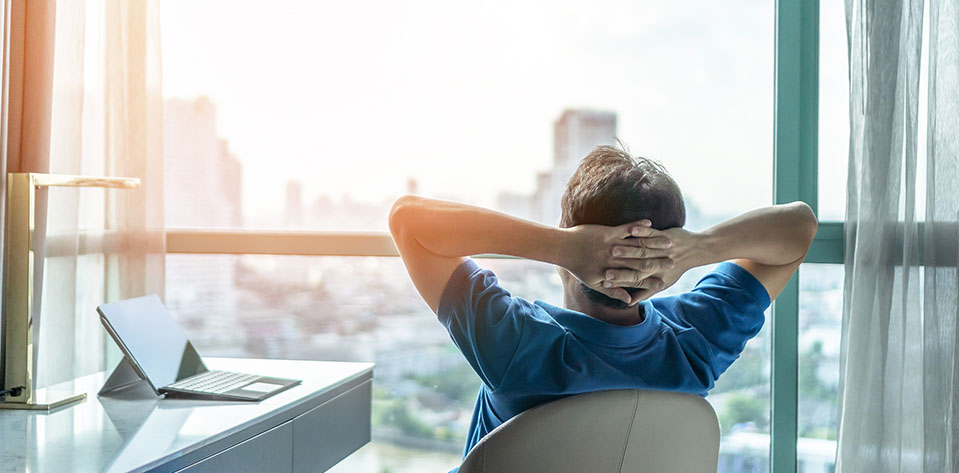 A man takes a break in his office during a stressful week, staring out the window relaxing.