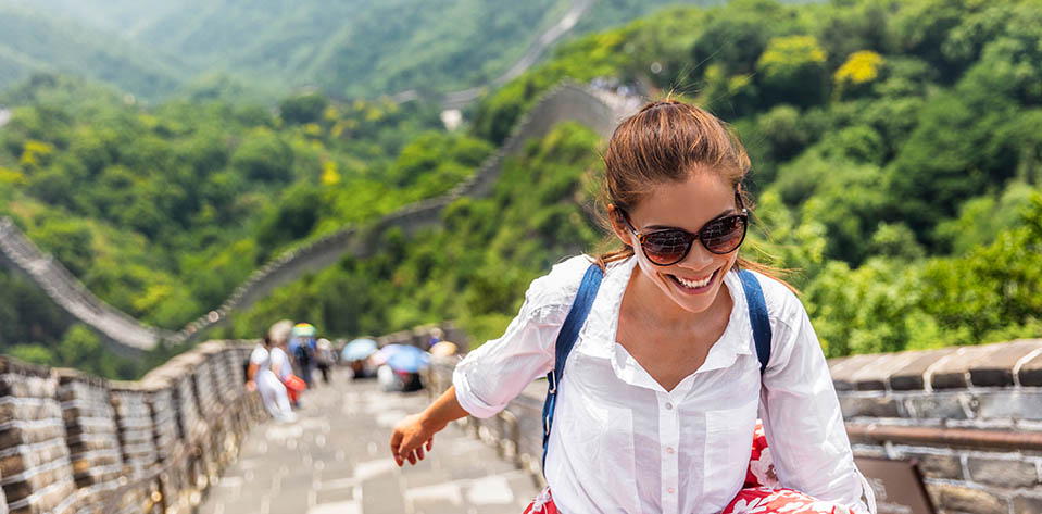 A woman walks up the great wall of china, smiling and alleviating stress by getting away on vacation.