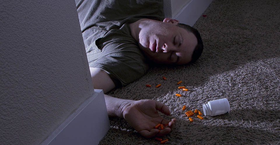 Dangers of Overdose - A young man lies next to a spilled open pill bottle on the floor of his home after an accidental overdose, an obvious sign of substance abuse.