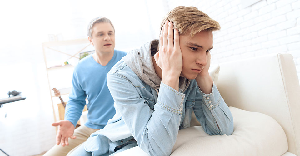 A son turns his back to his dad and covers his ears with his hands. Not wanting to listen to his dad lecture him about his drug use.