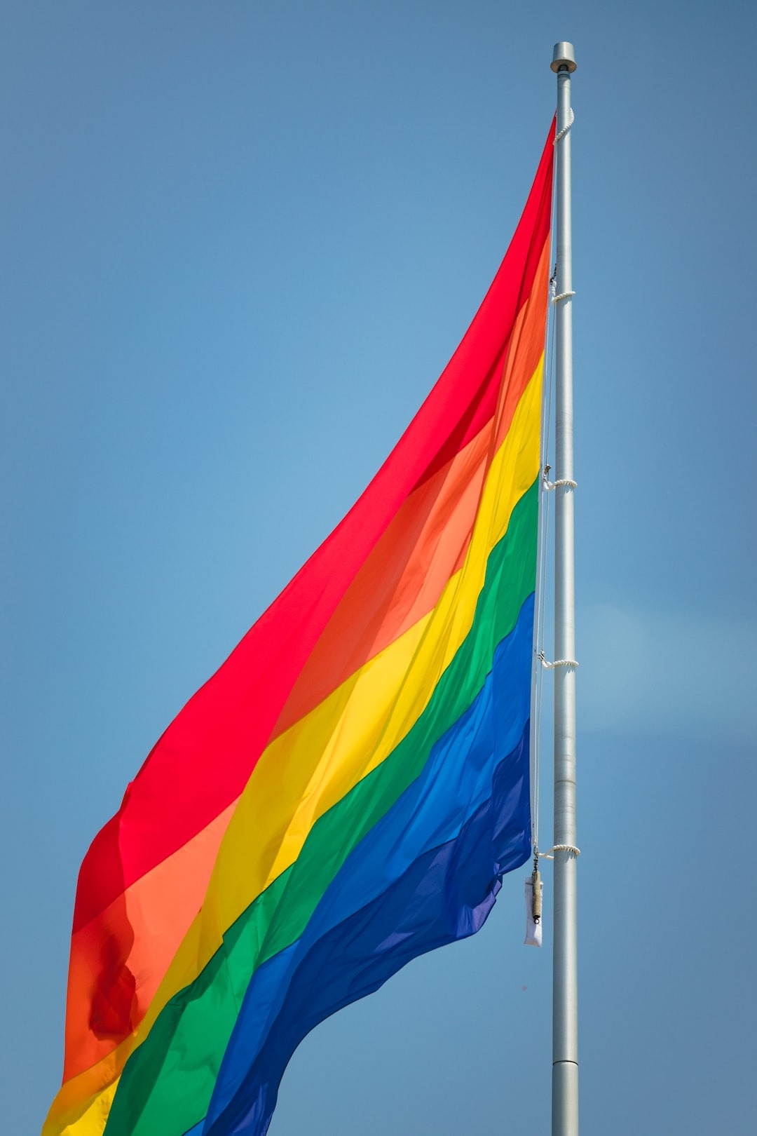Rainbow LGBTQIA+ pride flag waving against a clear blue sky, symbolizing inclusion and support