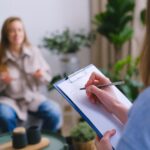 Therapist taking notes on clipboard while patient talks during a counseling session, illustrating support in a Partial Hospitalization Program (PHP)