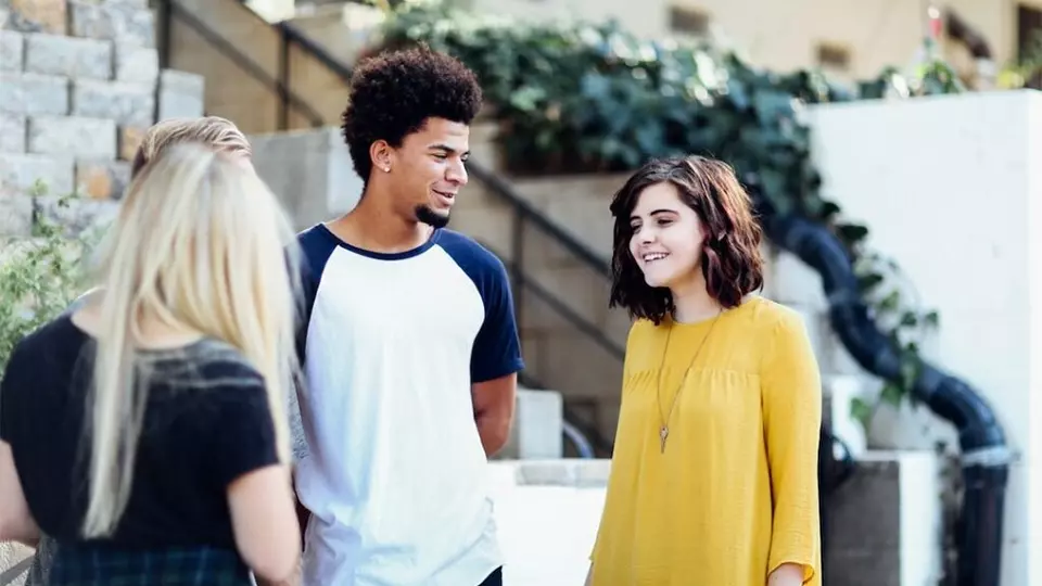 Young adults stand outside their outpatient treatment program chatting with each other.