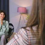 A young woman smiles and clasps her hands while speaking with a therapist during a one-on-one counseling session, symbolizing progress through individualized treatment for dual diagnoses.
