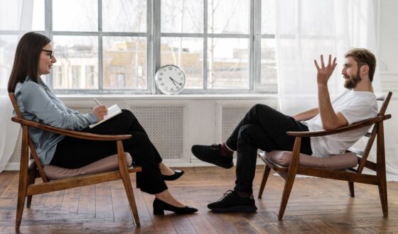 Male client talking to female therapist during one-on-one DBT session in a modern counseling room with large window
