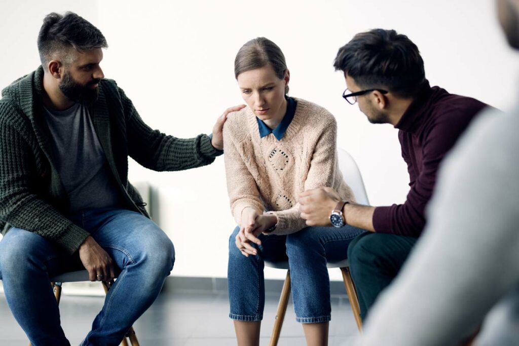 Two men supporting depressed woman during group therapy session.