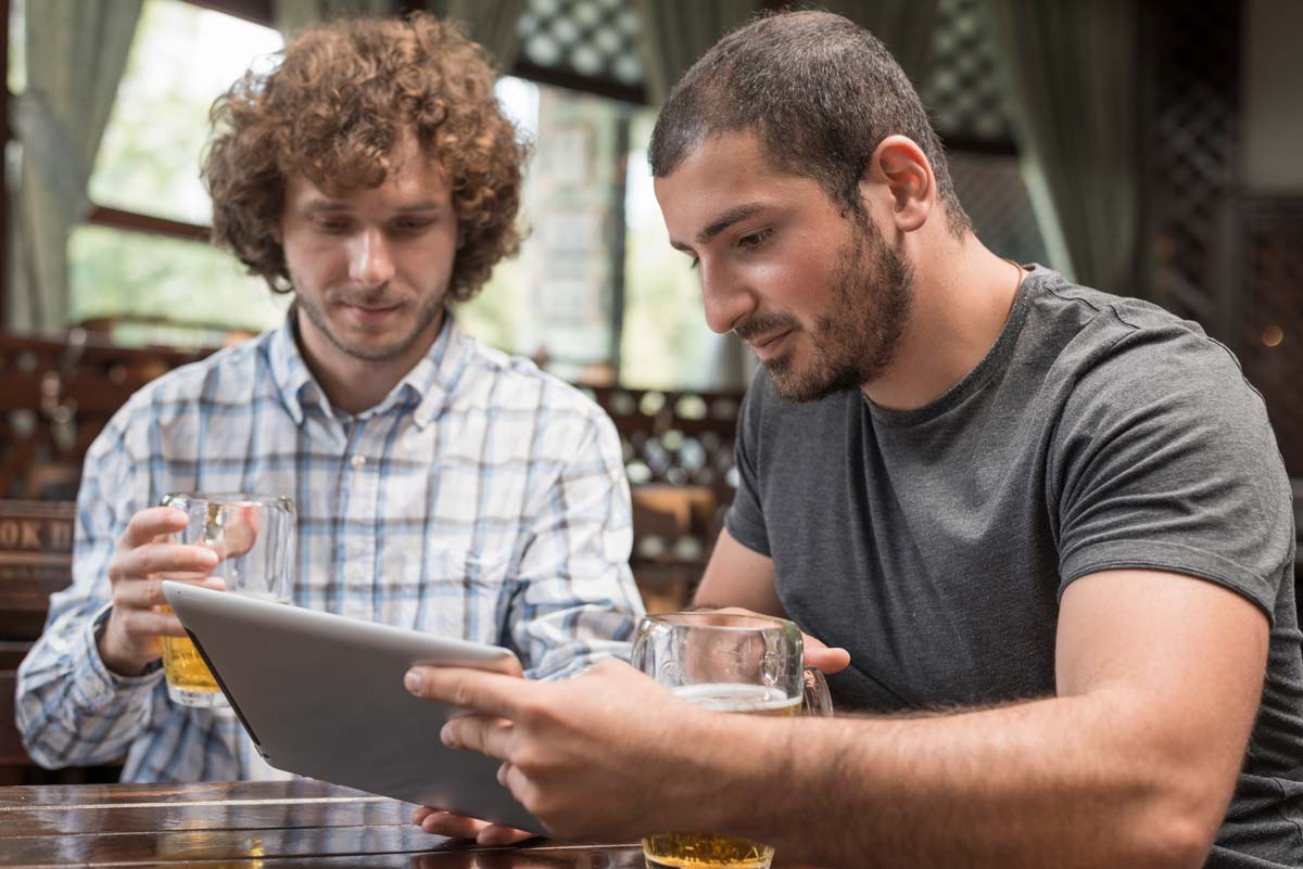 Man talking to his friend while having an alcoholic drink holding tablet