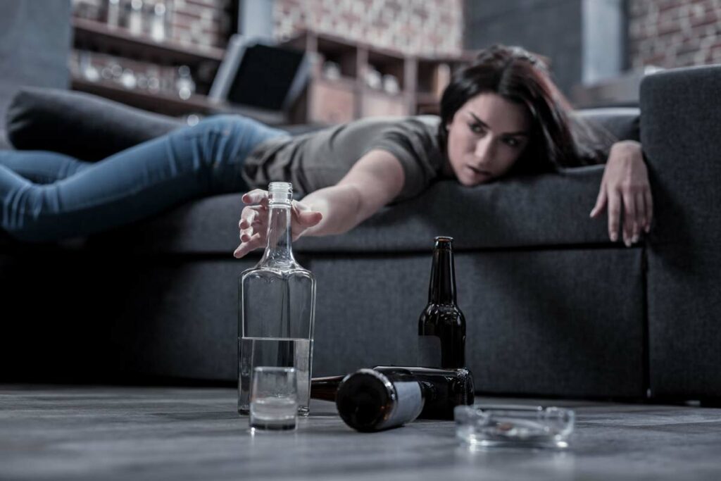 I need this drink. Selective focus of a half empty vodka bottle being taken by a drunken young woman while having a hangover