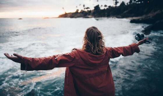 Person standing at the edge of the ocean with arms outstretched, symbolizing freedom, recovery, and hope after out-of-state addiction treatment.