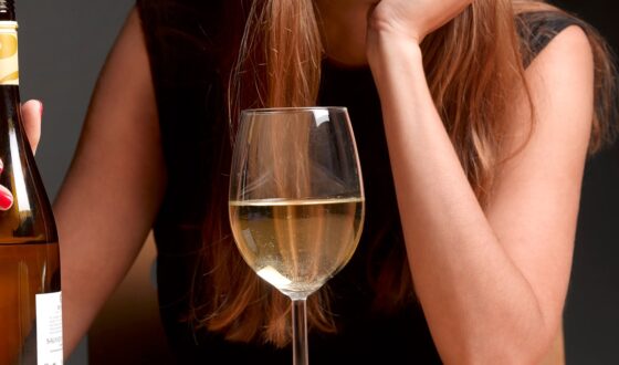 Woman holding a bottle of white wine with a full glass in front of her, representing potential signs of alcohol dependence and clear liquor addiction.
