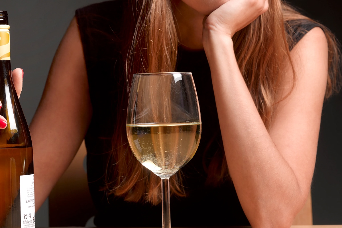 Woman holding a bottle of white wine with a full glass in front of her, representing potential signs of alcohol dependence and clear liquor addiction.