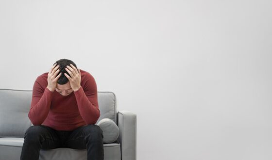 Stressed man sitting on couch holding head, showing early signs of needing professional mental health treatment at 12 South Recovery.