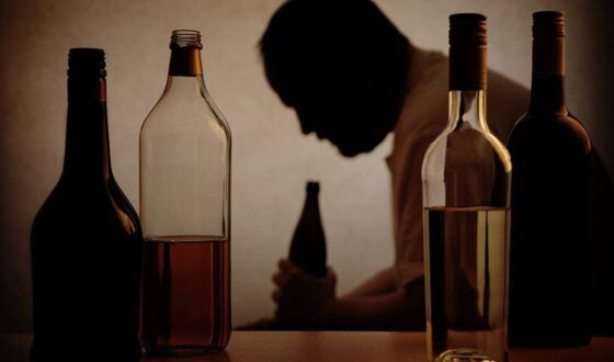 Silhouette of a man holding a bottle surrounded by liquor bottles, representing dark liquor and alcohol addiction and the increased risks of heavy drinking discussed by 12 South Recovery in Orange County, CA.